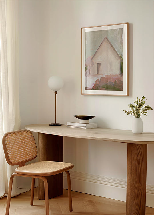 un espace de travail moderne et minimaliste avec un bureau en bois, une chaise tressée, une lampe et une peinture encadrée d'une maison.
