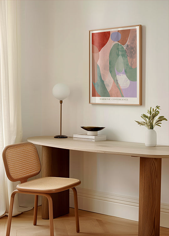 un espace de travail minimaliste avec un bureau en bois, une chaise tressée, une lampe et une peinture abstraite encadrée au mur.