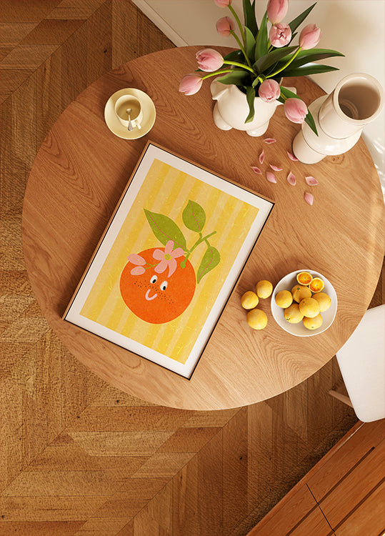 une table en bois avec une image encadrée d'une orange, un bol de citrons, un vase de tulipes roses et une bougie dessus.