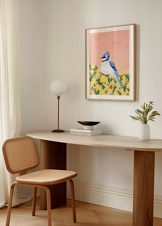 un coin confortable d'une pièce avec un bureau en bois, une chaise tressée, une lampe et une photo encadrée d'un oiseau bleu sur fond jaune.