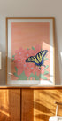 une peinture encadrée représentant un papillon sur une fleur rose, exposée sur une armoire ou une étagère en bois.