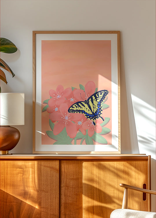 une peinture encadrée représentant un papillon sur une fleur rose, exposée sur une armoire ou une étagère en bois.