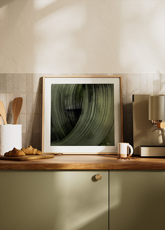 une photographie encadrée d'une feuille verte sur un comptoir de cuisine, avec une cafetière et d'autres articles de cuisine visibles en arrière-plan.