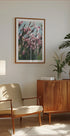un salon confortable avec une armoire en bois, un fauteuil beige, une photo encadrée de fleurs roses et une plante en pot.