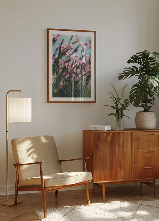 un salon confortable avec une armoire en bois, un fauteuil beige, une photo encadrée de fleurs roses et une plante en pot.
