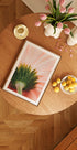 une table en bois avec une photo encadrée d'une fleur, un bol de fruits et un vase de fleurs roses.