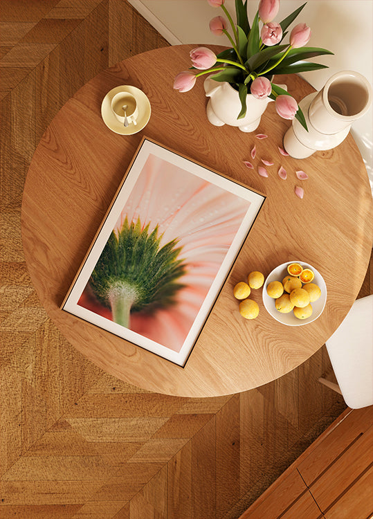 une table en bois avec une photo encadrée d'une fleur, un bol de fruits et un vase de fleurs roses.