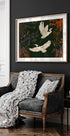 un canapé noir et blanc avec une couverture blanche et deux oreillers blancs, posé contre un mur sombre avec une peinture encadrée de deux oiseaux blancs en vol au-dessus.