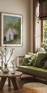 un salon confortable avec une grande fenêtre, un canapé vert, une table basse en bois et une peinture encadrée d'une maison.