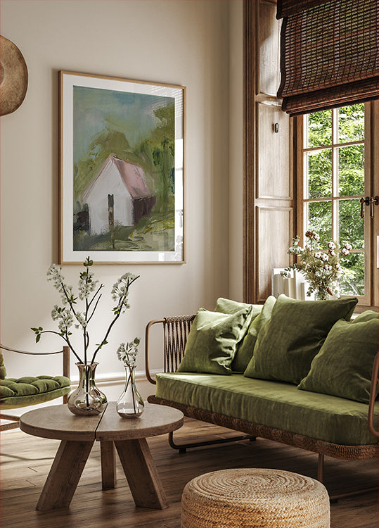 un salon confortable avec une grande fenêtre, un canapé vert, une table basse en bois et une peinture encadrée d'une maison.