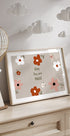 Une impression encadrée avec un motif floral et le texte « Baby You are Magic » est exposée sur une commode en bois, avec une lanterne décorative en papier suspendue au-dessus.