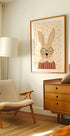 un salon cosy avec un fauteuil beige, une commode en bois et une photo encadrée d'un lapin portant des lunettes.