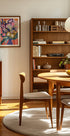 un salon cosy et bien organisé avec une étagère en bois, une table ronde en bois et une chaise en bois. La pièce dégage une atmosphère chaleureuse et accueillante, avec un tableau au mur et un bol de fruits sur la table.